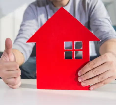 holding up a red house paper cut out with a thumbs up